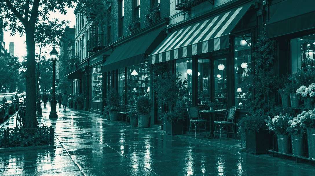 A row of storefronts with striped canvas awnings along a rain-washed sidewalk